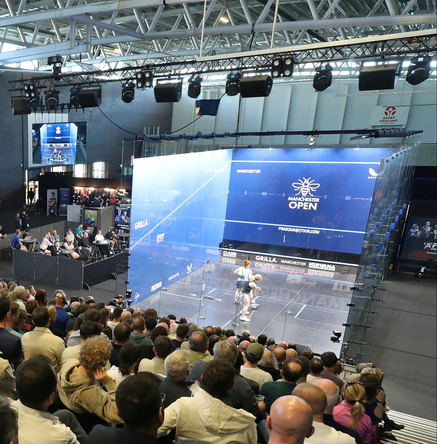 Audience watching a squash match at the Manchester Open event inside a large indoor arena.